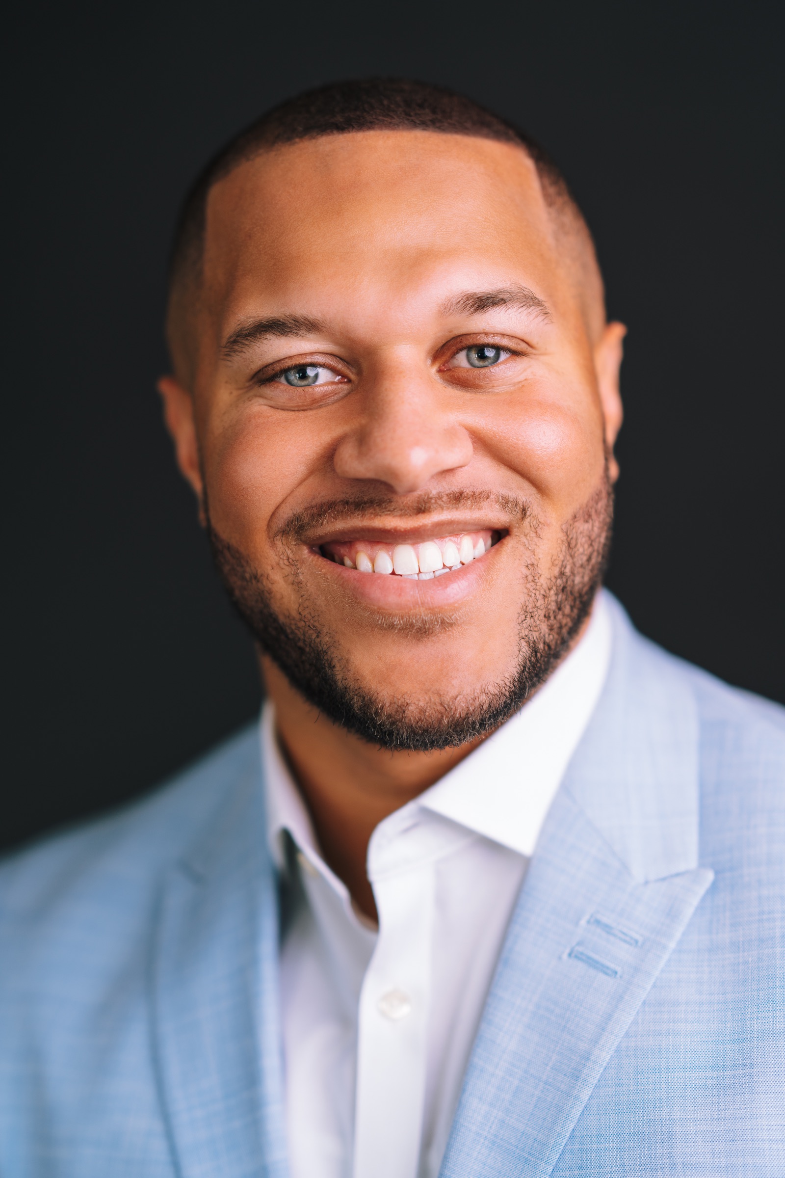Smiling professional in a light blue suit photographed against a dark background