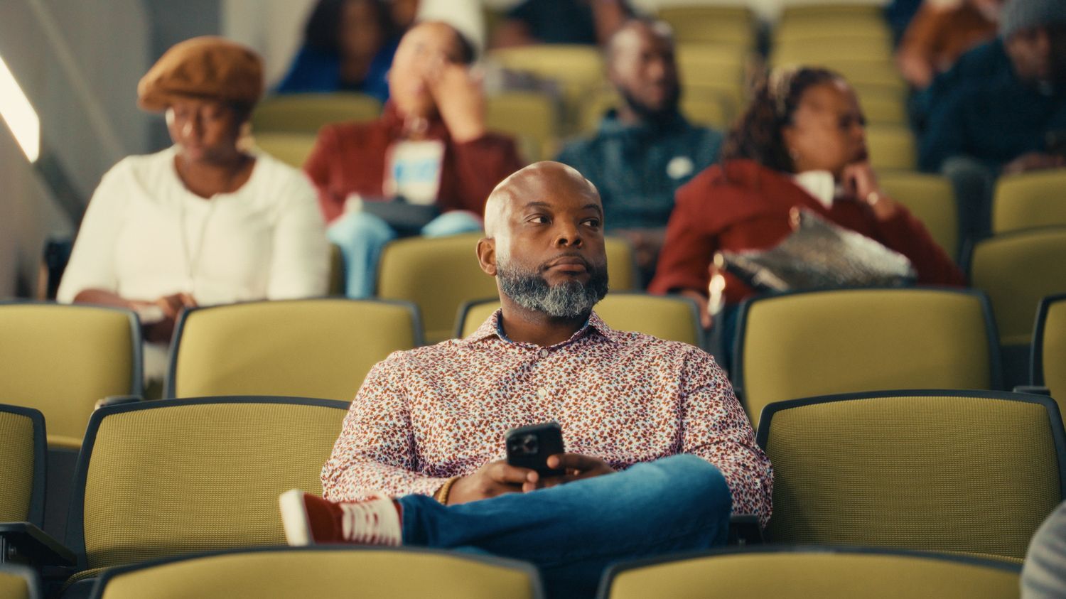Film still of a founder seated in an auditorium