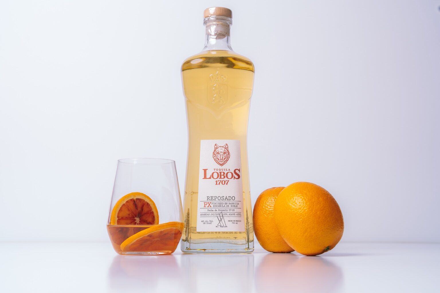 Studio product photograph of a bottle, glass, and oranges