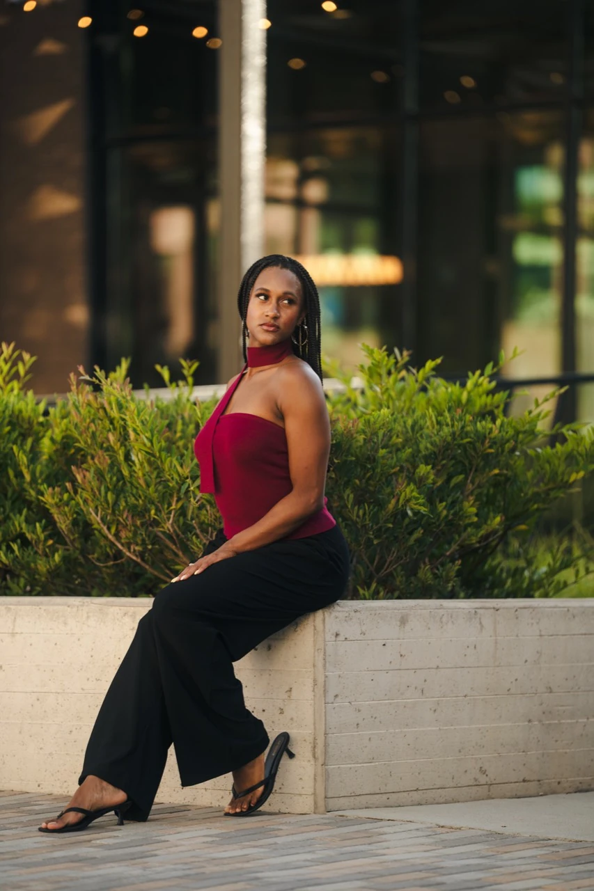 Jasmine Neely seated on a stone ledge in a burgundy outfit